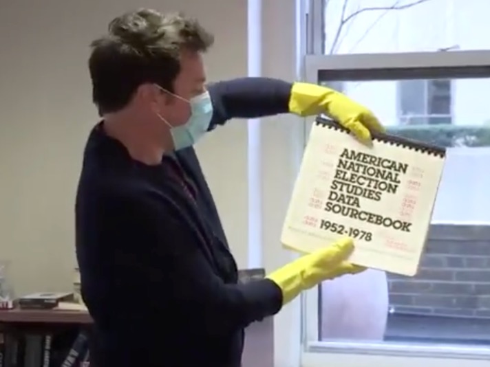 Jimmy Fallon in cleaning gloves holds up the American National Election Studies Data Sourcebook 1952-1978
