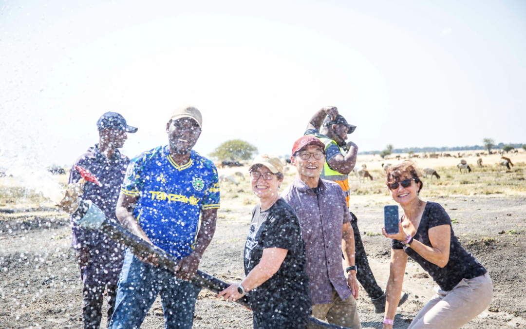 5 members of the Bold Challenges Team holds a pipeline hose and smile for the camera in the water spray