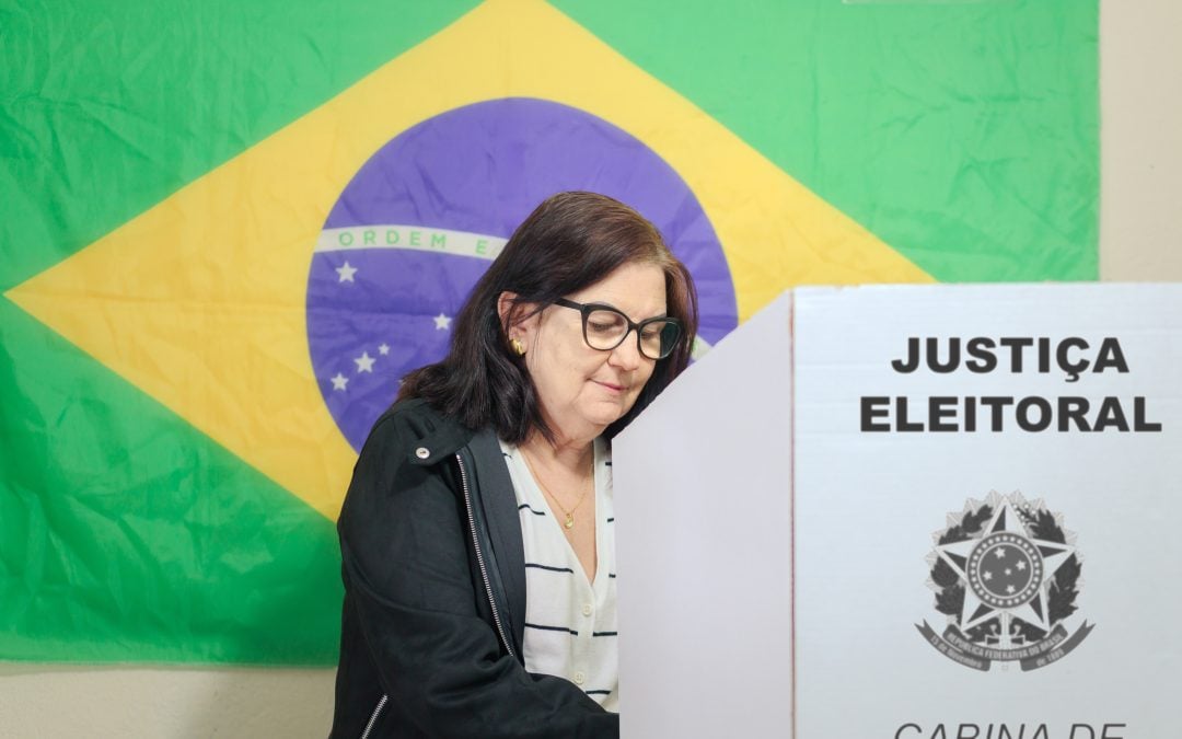 Brazilian woman casting a ballot in front of a Brazilian flag